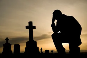 Silhouette of a man kneeling among gravestones at sunset
